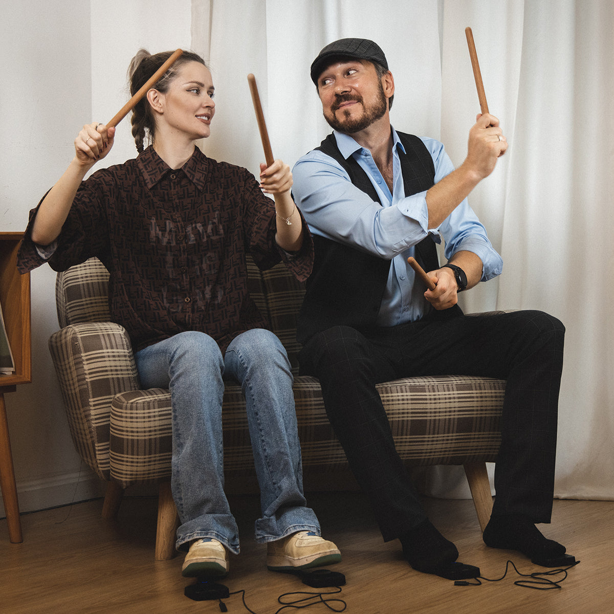 A man and a woman using the compact PocketDrum on chairs indoors